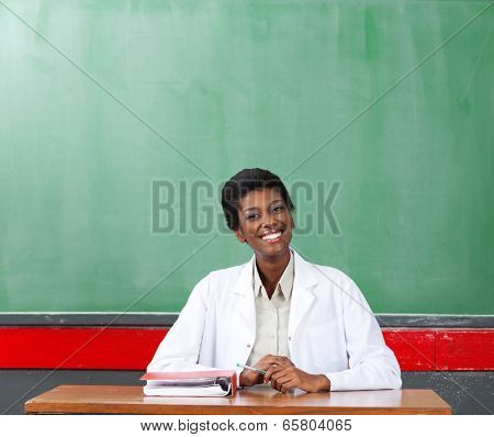 Portrait of happy African American female teacher sitting at desk in classroom