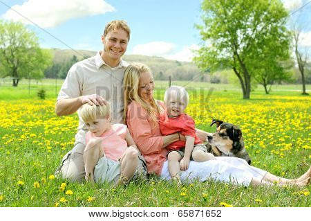 Happy Family Relaxing Outside In Field Of Flowers With Dog