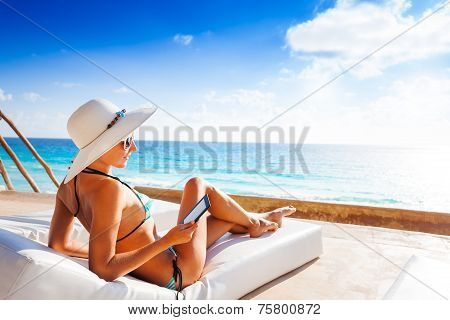 Young woman with hat laying and reading e-book