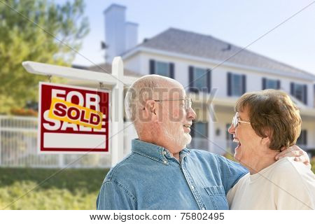 Happy Affectionate Senior Couple Hugging in Front of Sold Real Estate Sign and House.