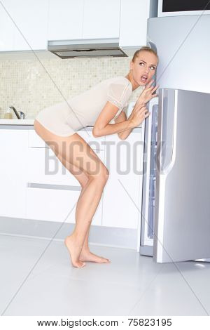 Indecisive slender young woman in her sleepwear raiding the fridge as she looks for a midnight snack looking thoughtfully into the air