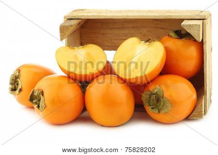 fresh kaki fruit and a cut one in a wooden crate on a white background