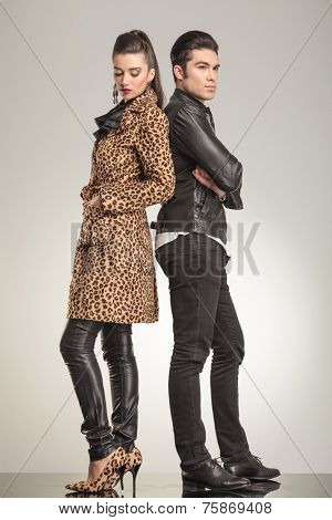 Full body image of a young fashion couple looking away from the camera. The woman is holding her hands in pockets while the man si haolding his arms crossed.