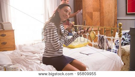 Woman Putting On Make Up And Man Getting Dressed In Bedroom