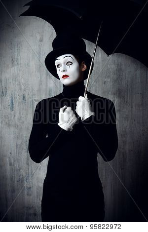 Portrait of a male mime artist standing under umbrella expressing sadness and loneliness. Grunge background.