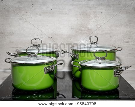 Four green enamel stewpots on black induction cooker