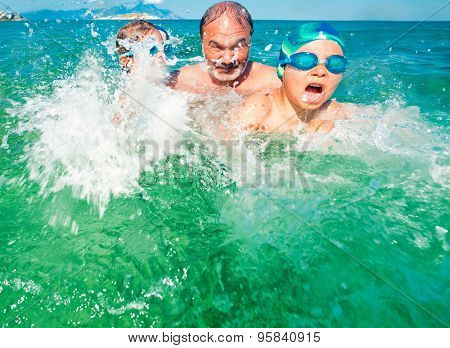 Grandfather with his grandson and granddauther playing in the sea, splashing water all arround.