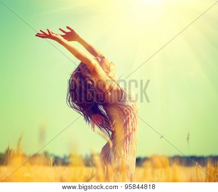 Beauty Girl Outdoors enjoying nature on wheat field. Beautiful Teenage Model girl with long hair raising hands on golden Field, Sun Light. Glow Sun. Free Happy Woman. Toned in warm colors