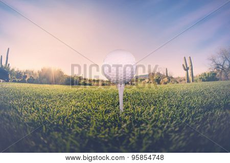 Super wide angle view of golf ball on tee with desert fairway and stunning Arizona sunset in background