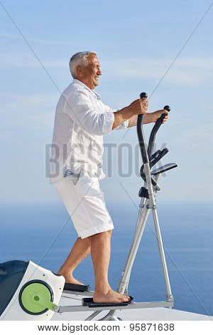 healthy senior man working out on gym treadmill machine at modern home terace with ocean view