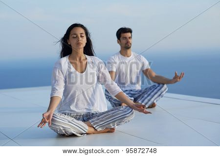 young couple practicing yoga at sunset in modern home terace with ocean and sunset in background