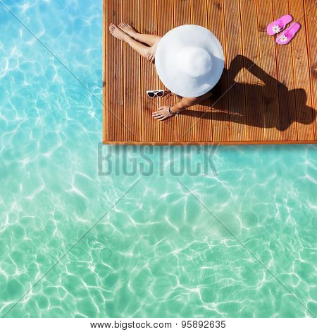 Summer holiday fashion concept - tanning woman wearing sun hat at the pool on a wooden pier shot from above