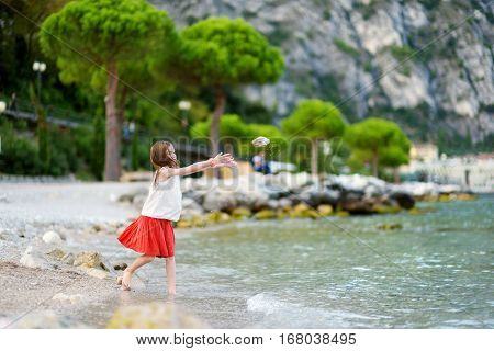 Two Cute Little Sisters Having Fun On A Beach Of Limone Sul Garda, A Small Town And Comune In The Pr