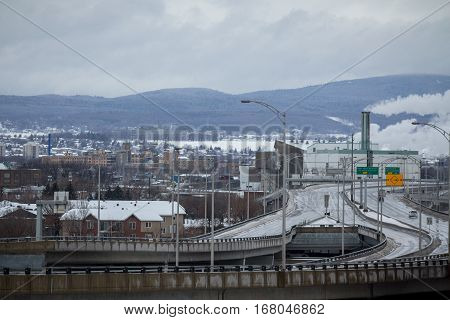 Typical North America Expressway in winter on a cloudy day with a fuming factory on the background in Quebec City, QC, Canada