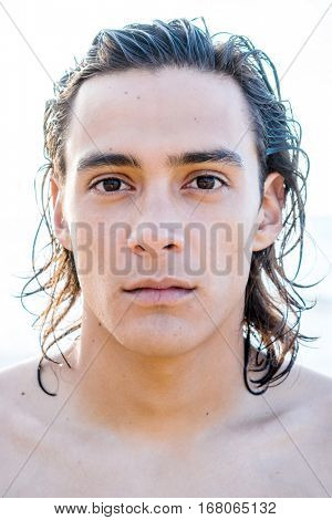 Close-up portrait of handsome young guy with wet long dark hair without a shirt looking at camera