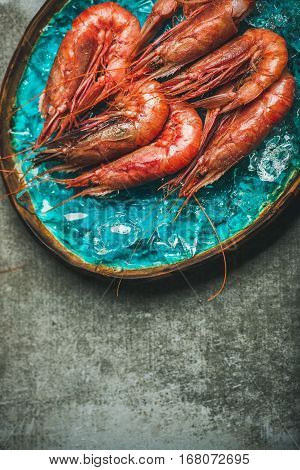 Raw uncooked red shrimps on chipped ice in turquoise blue ceramic tray over grey concrete background, top view, copy space, vertical composition. Fresh seafood concept