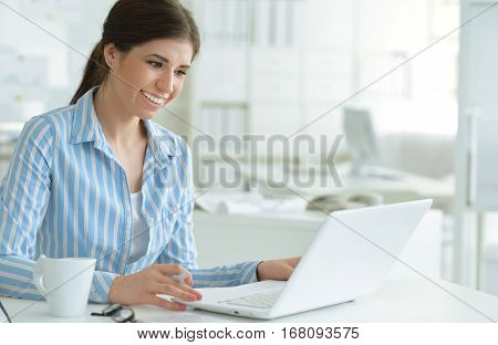 Portrait of a young female office worker, using laptop
