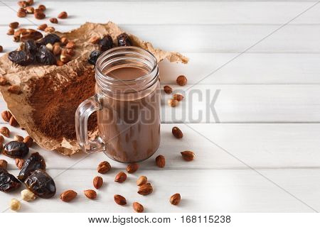 Detox cleanse drink, chocolate smoothie ingredients. Natural, organic healthy juice in glass jar for weight loss diet or fasting day. Cocoa powder, nuts, date fruit mix on white wood with copy space