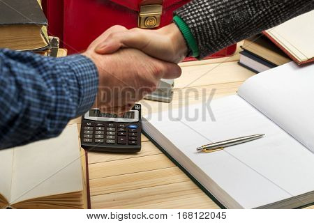 Business concept. Business partners handshaking after signing contract. Pertnership. On a wooden table books, documents, calculator, red briefcase