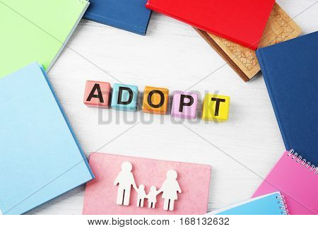 Colorful cubes with word ADOPT, figure in shape of family and notepads on wooden background