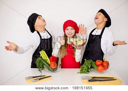 three young chefs near the white table evaluate a salad isolated. godlike