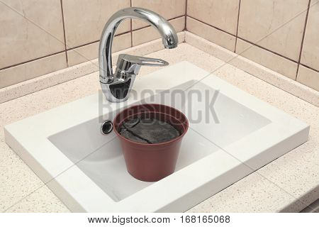 Water shortage concept. Pot with dry ground in white sink