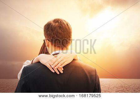 Romantic couple in love on Happy valentines day. Lovers back hugging and standing on tropical beach with dramatic sunset sky background. Girl wearing engagement heart shape ring. Relationship concept.