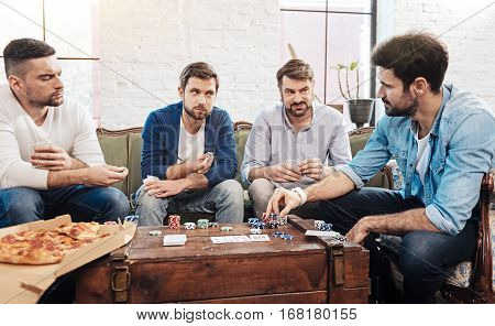 Do not try cheating. Serious handsome nice men holding cards and looking at their friend while playing the poker game