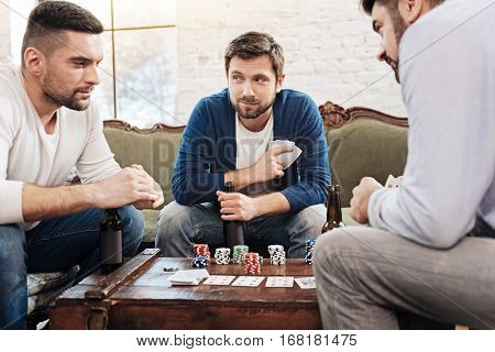 Dishonest play. Attractive good looking bearded man holding his cards and having a sly look while playing the poker game