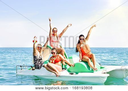 Happy young women having fun raising arms smiling on rental pedalos in blue ocean - Best female friends boat party and sunny joyful moment together - Concept of summer holiday and teenage friendship