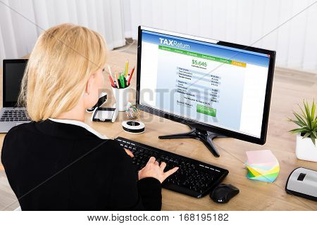 Close-up Of A Young Businesswoman Calculating Tax On Office Desktop