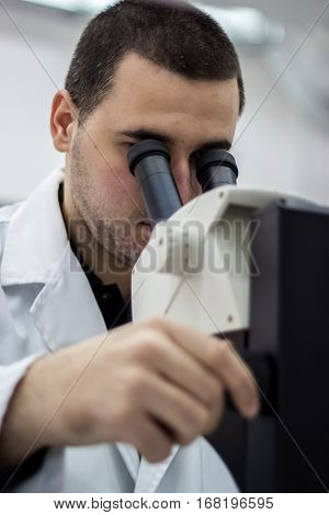 Female Medical Or Scientific Researcher Man Doctor Looking Through A Microscope In A Laboratory. You