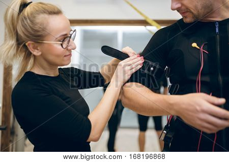 Young Woman Fastening Belt Of Ems Suit On Man Arm