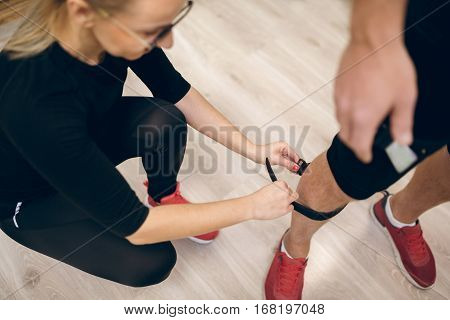Female Trainer Fastening Belt On Man Leg