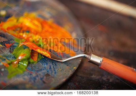 Preparing for creation. Close up of a putty knife and orange and green paints lying on a palette.