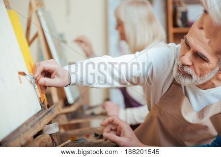 Do it together. Concentrated talented elderly man painting with his colleague while working and enjoying their hobby