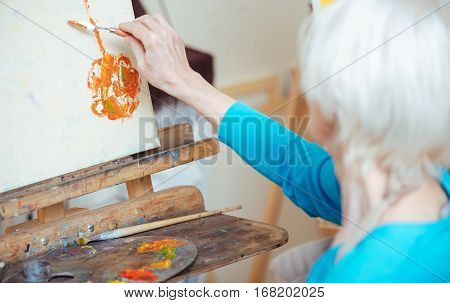 Delicious painting. Female elderly concentrated artist painting picture and using putty knife while working in studio.