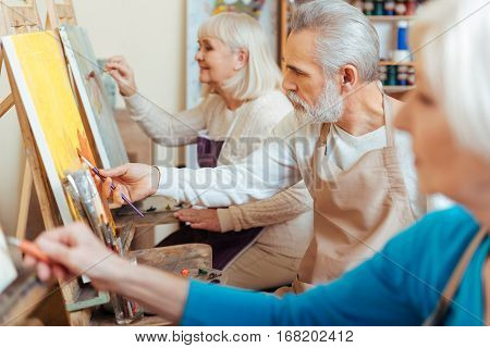 Productive cooperation. Three professional talented elderly artists spending time in painting studio while painting and enjoying their hobby