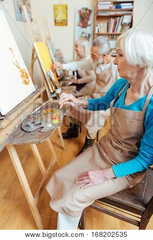 Happy colleagues. Three professional delighted elderly artists spending time in painting studio while painting and enjoying their hobby.