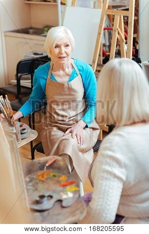 Common activity. Elderly happy ambitious ladies talking and spending time in painting class while drawing.