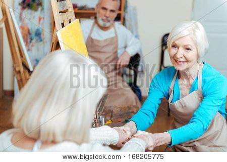 Friendly colleagues. Elderly happy female artists talking and laughing in painting class while drawing.