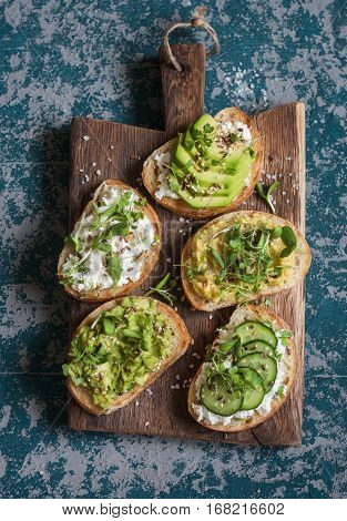 Healthy sandwiches with avocado hummus ricotta cucumber sunflower sprouts micro greens and flax seeds. On a wooden cutting board top view. Healthy vegetarian snack