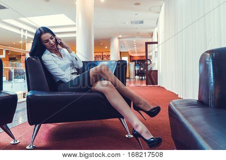 Stylish girl talking on a smartphone sit on a sofa in the hall of the hotel