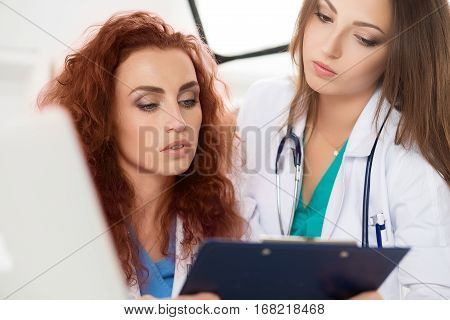 Two female doctors looking at clipboard with patient information form discussing his diagnosis and treatment. Health care medical education and service concept.