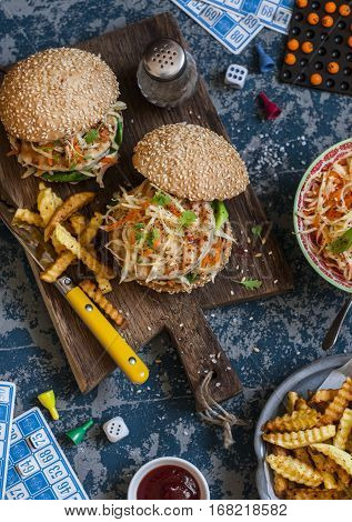 Hamburgers with grilled chicken and cole slaw on a wooden board on the table with cards and bingo chips top view. Flat lay