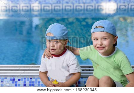 Two adorable sibling kids hugging and having fun outdoors. Cute brothers playing together on sunny warm summer day. Brother love. Happy boys smiling on a sunny day by the pool. Brothers portrait