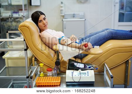 Donor of blood gripping special flexor while sitting in armchair