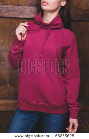 Young woman wearing blank magenta sweatshirt with area for your logo or design, mock-up of template magenta sweatshirt, wooden wall in the background
