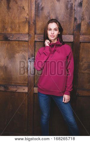 Young woman wearing blank magenta sweatshirt with area for your logo or design, mock-up of template magenta sweatshirt, wooden wall in the background