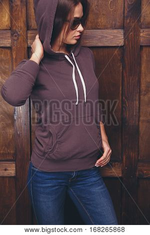 Young woman wearing blank brown sweatshirt with area for your logo or design, mock-up of template brown sweatshirt, wooden wall in the background
